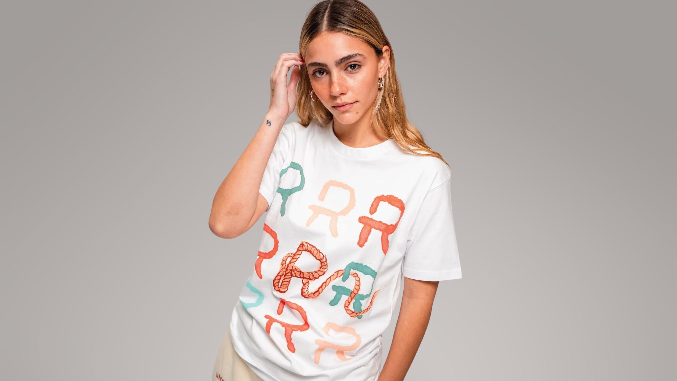 a woman wearing a white graphic tee with colorful letters and a lasso design by Ranchers