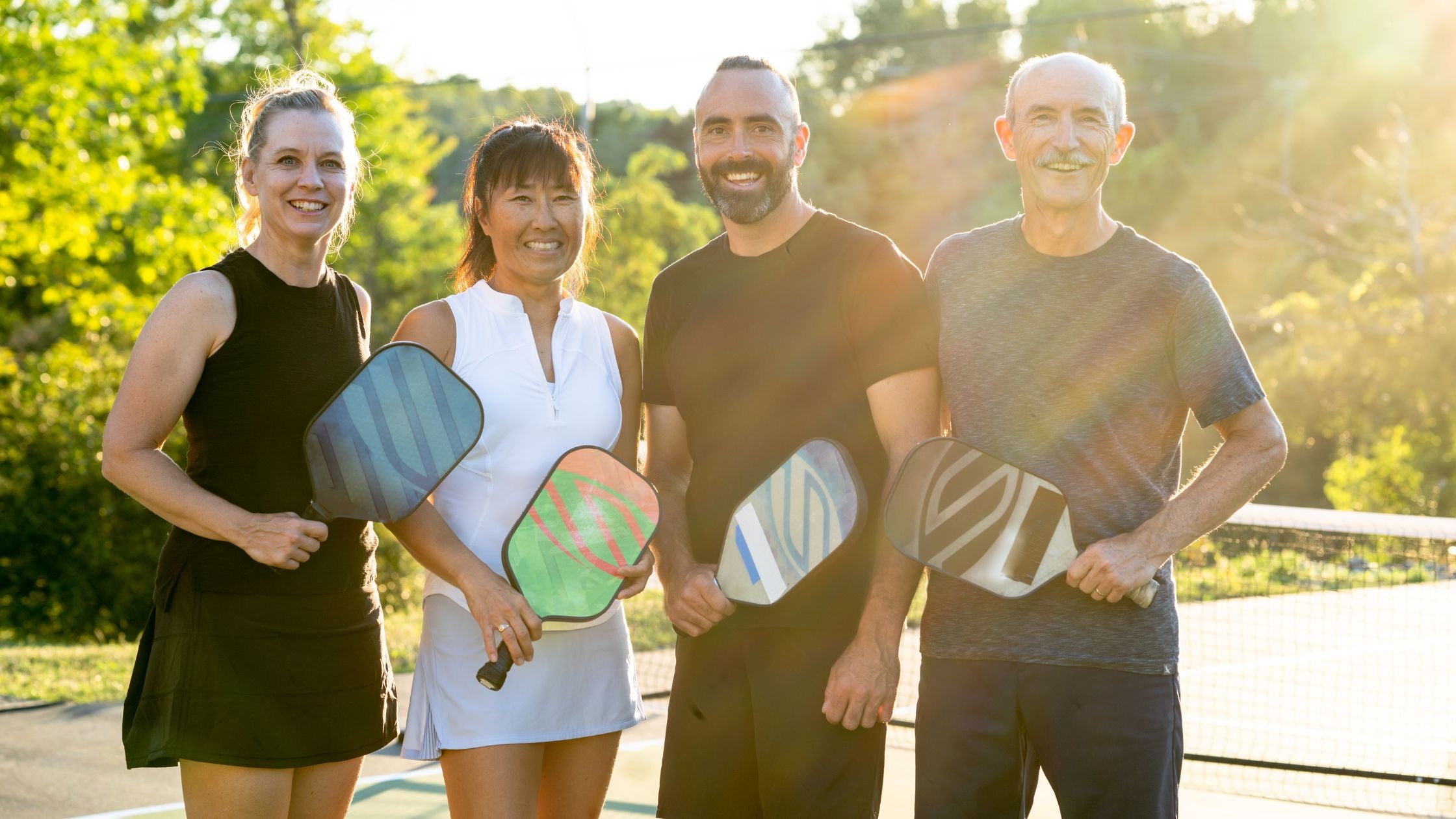 four people happily posing and holding pickleball paddles