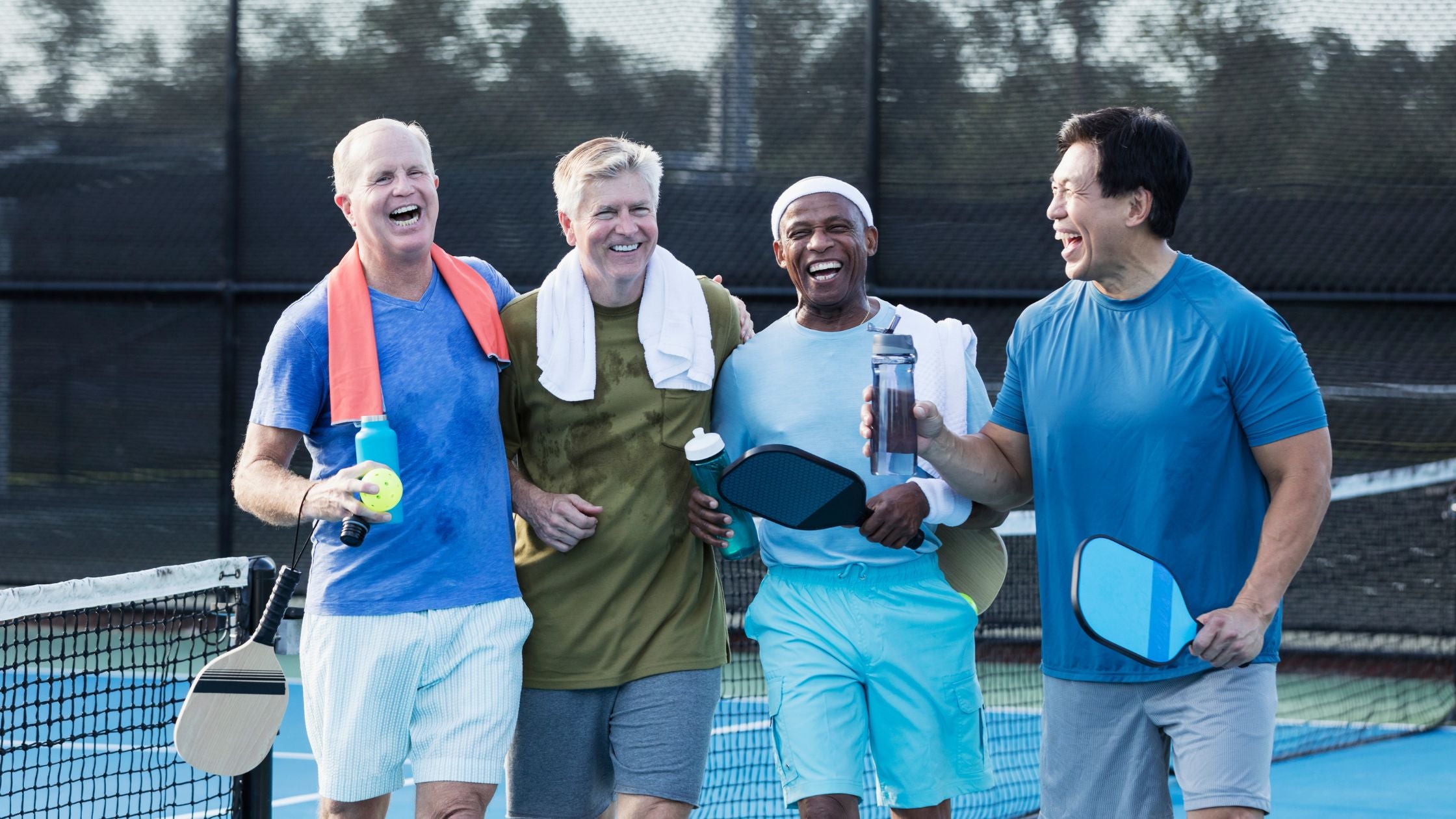 a group of four men smiling and holding pickleball paddles and water bottles