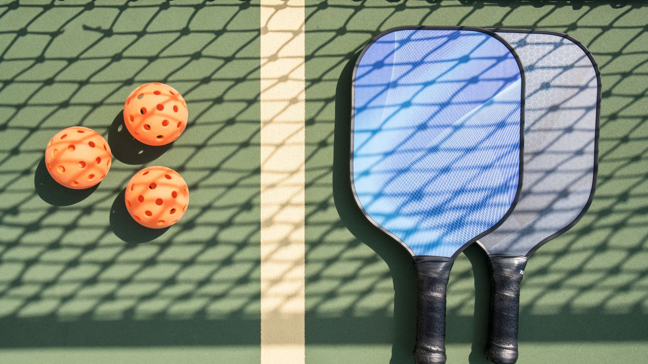 two pickleball paddles and balls on a green court