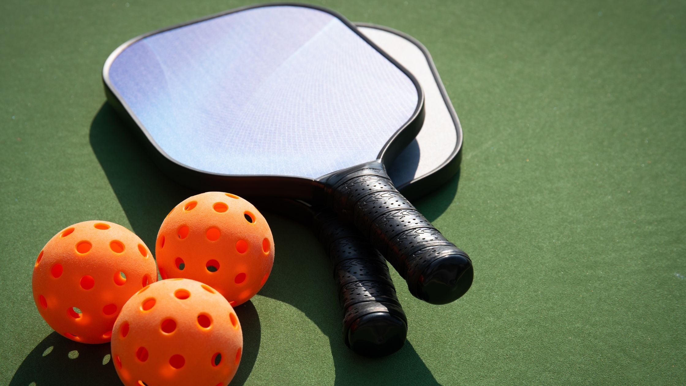 three pickleballs and two paddles placed on a green court