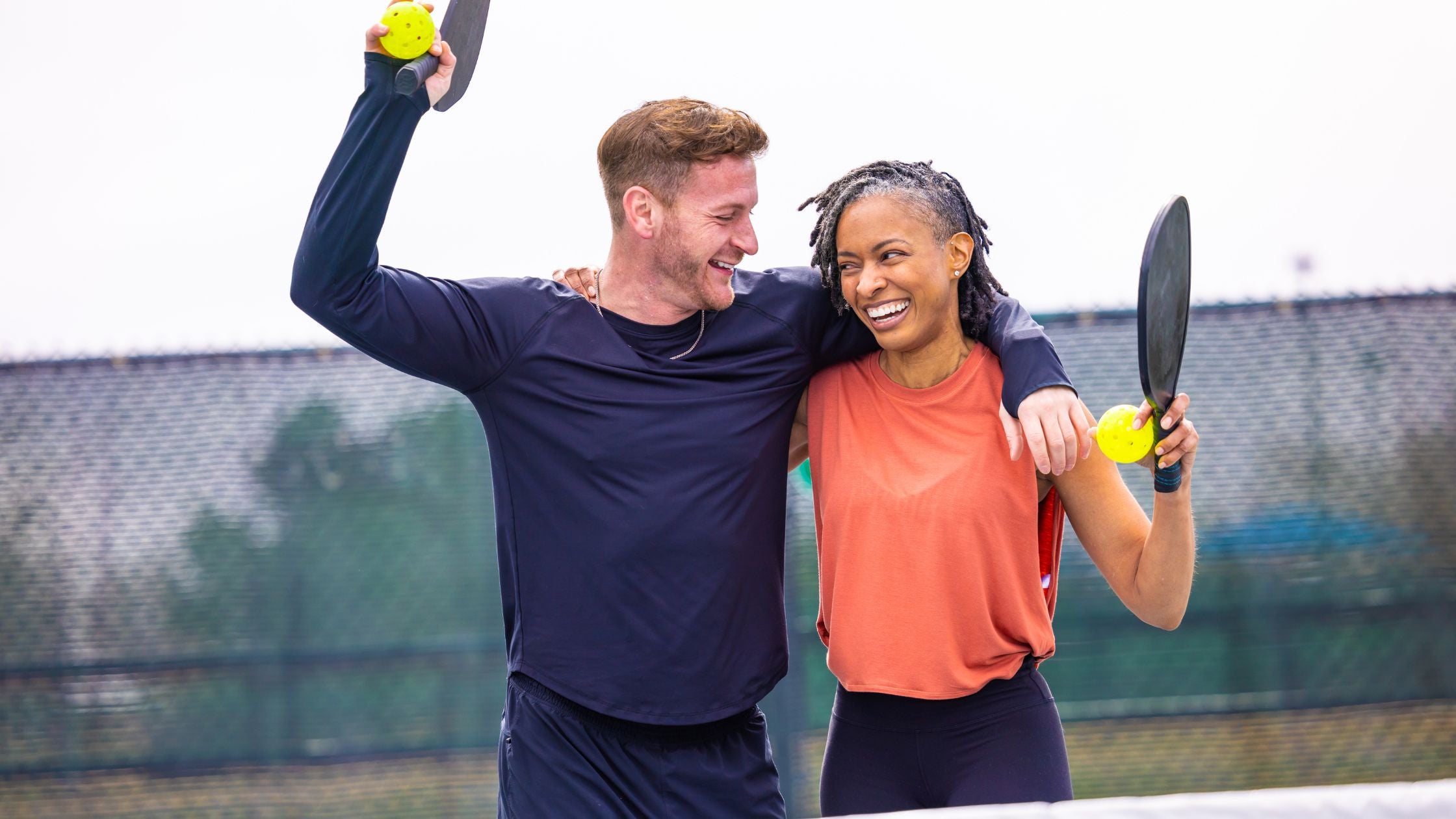 a man and woman smiling while holding a pickleball paddle and ball