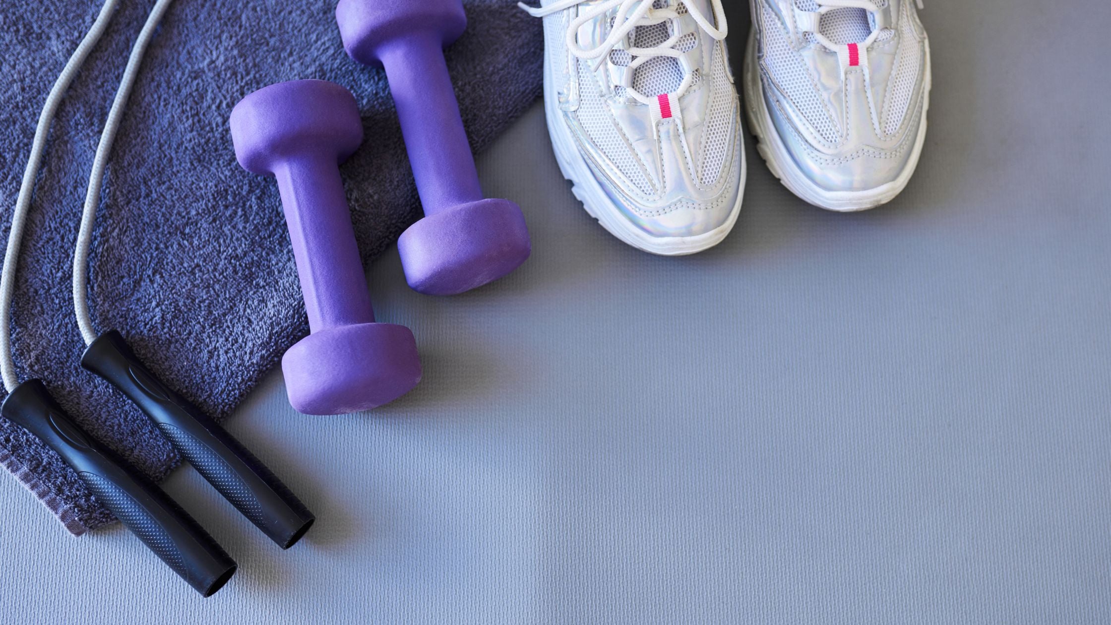 Purple dumbbells, a jump rope, and white sneakers on a gym floor