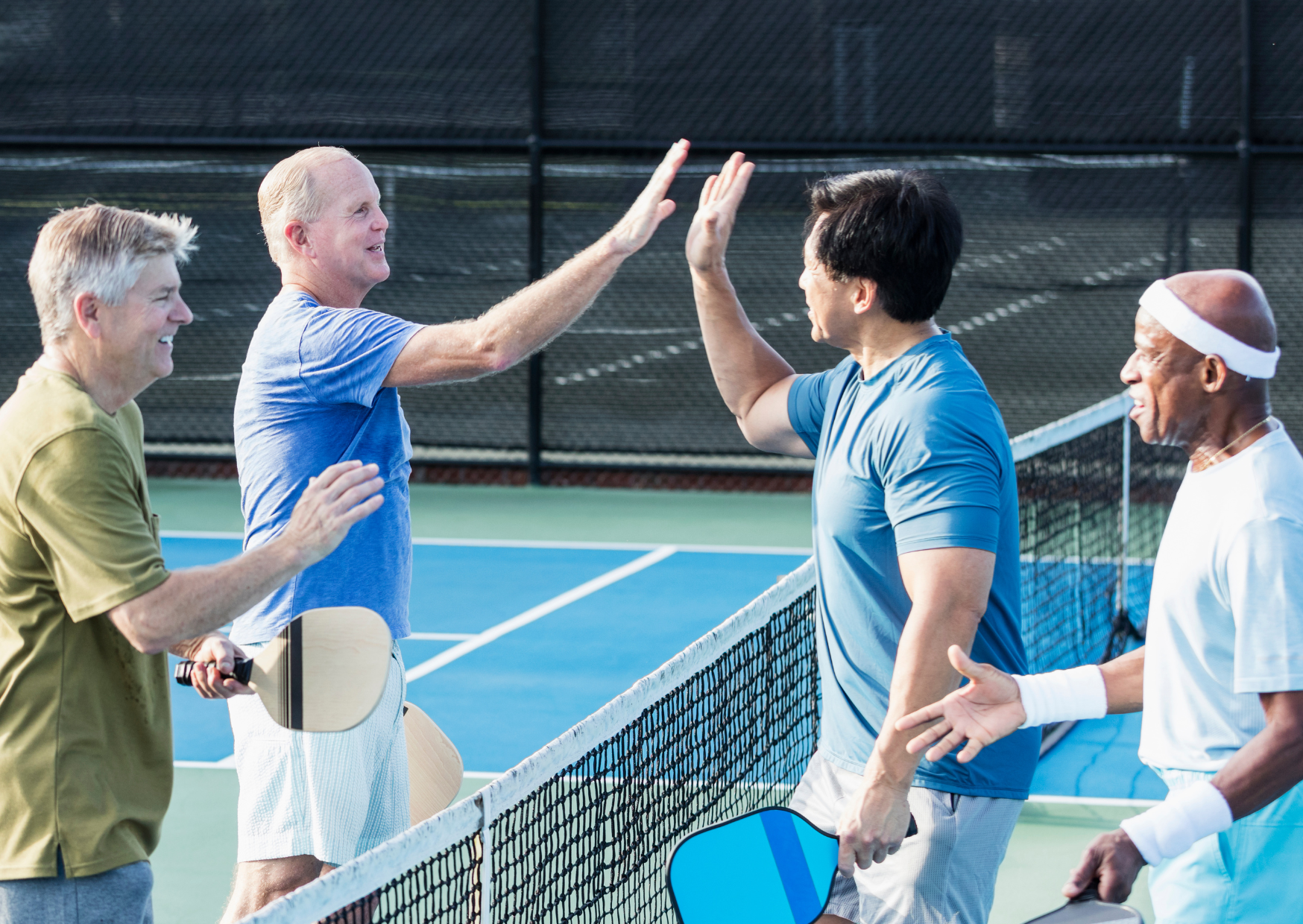 Four senior men playing pickleball and high-fiving on the court after a match